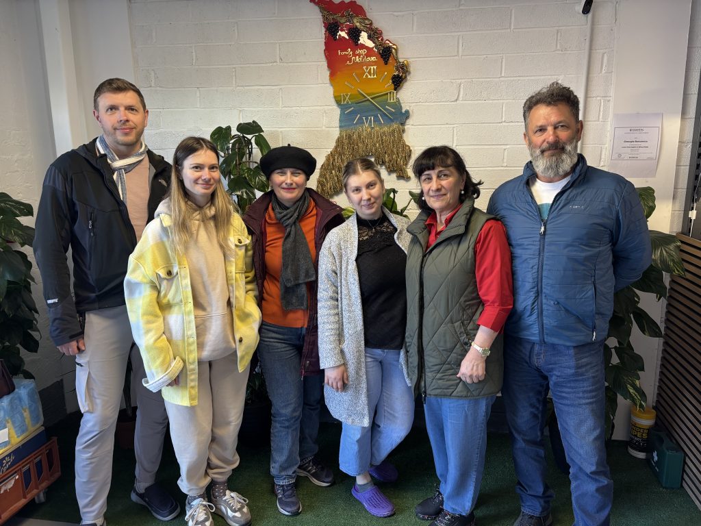There are 6 people in the foreground of the photograph and a clock in the shape of the Republic of Moldova in the background. The six people have attended Coffee with the Moldovan Diaspora Business Alliance event.