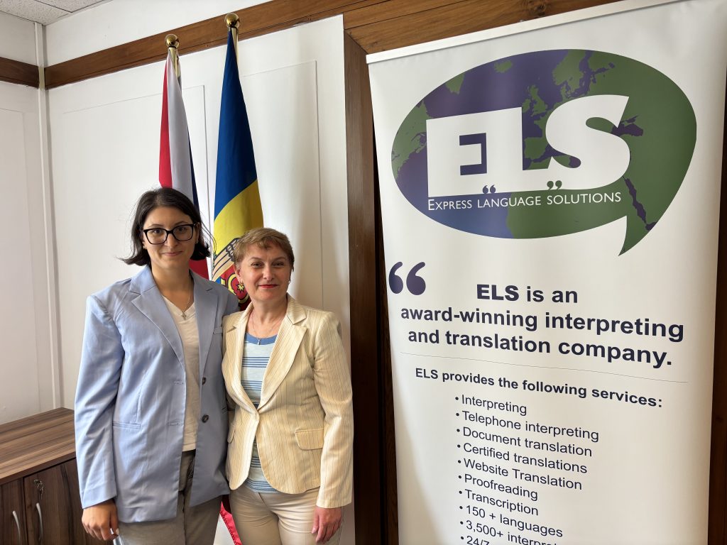 Dina Railean, Honorary Consul of the Republic of Moldova in Manchester, United Kingdom, and CEO of Express Language Solutions Ltd, stands alongside educator and Romanian GCSE advocate Alesea Tudosan during a meeting focused on promoting Romanian language education in UK schools. Behind them are the flags of the Republic of Moldova and the United Kingdom, together with an Express Language Solutions banner highlighting the company's interpreting and translation services. The meeting explored collaboration opportunities in support of the campaign to introduce Romanian as a GCSE subject and strengthen educational, cultural, and linguistic ties between the UK, Moldova, and Romania.